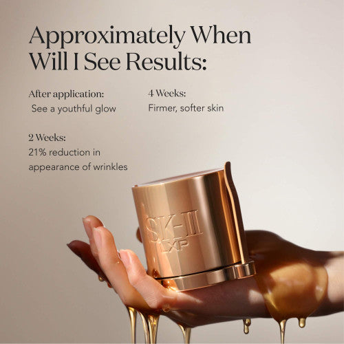 Hand holding SK-II LXP Ultimate Revival Cream jar with golden liquid dripping over fingers on a neutral background