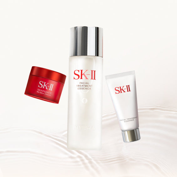 SK-II Pitera Youth Essentials Kit products including Facial Treatment Essence bottle, Skinpower cream jar, and cleanser tube arranged on a soft liquid-textured background