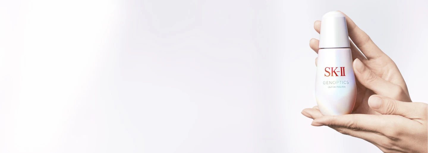 Hand holding a white skincare bottle with red logo on a light gray background