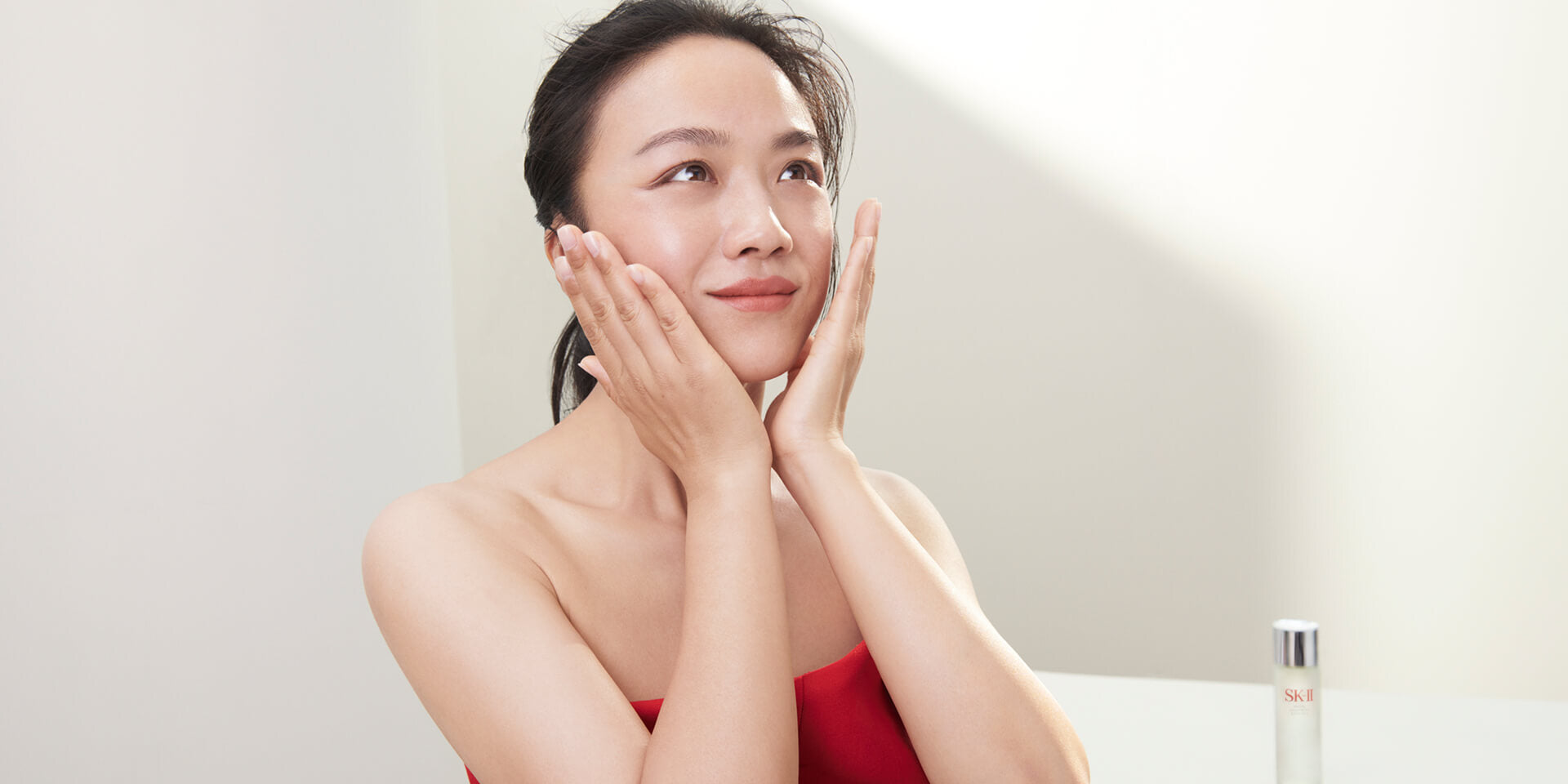 Close-up of face with hands on cheeks and product in background, representing skin spots and brightening skincare  