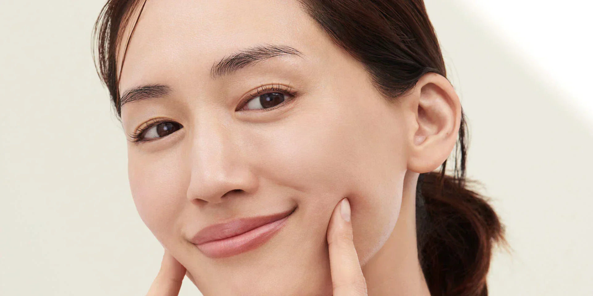 Close-up of face with fingers gently pressing cheeks, representing skincare routine in the 30s