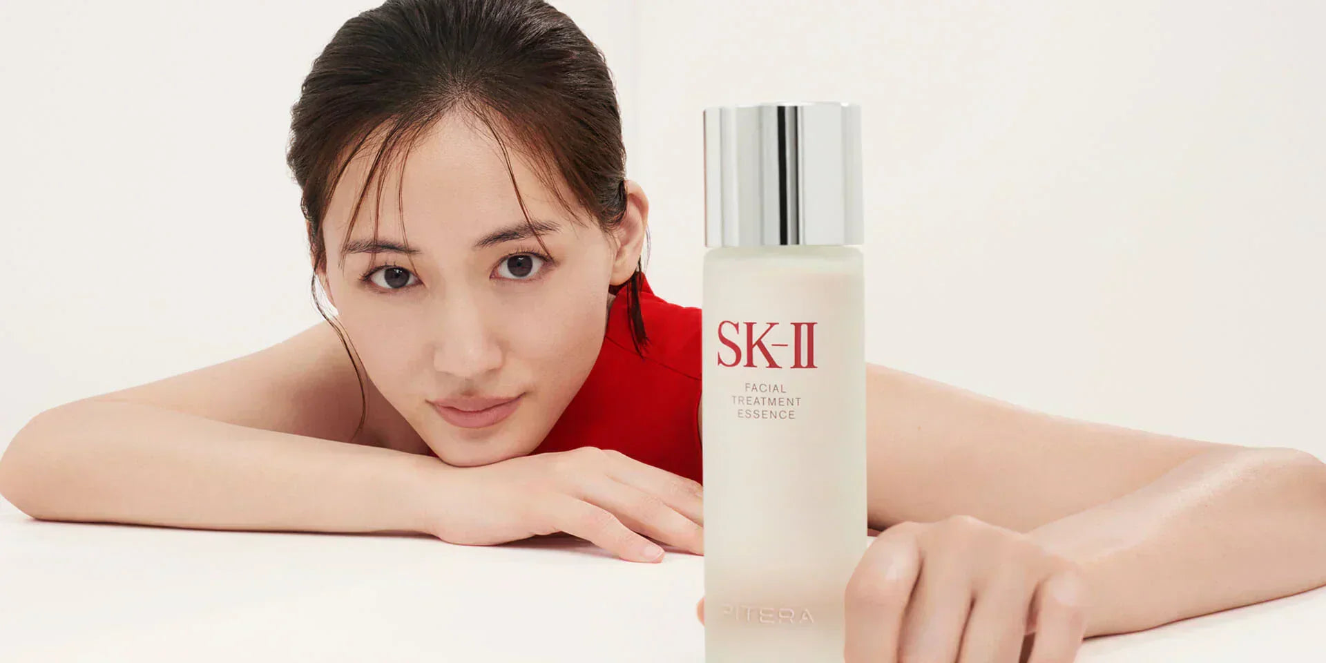Woman leaning forward with arm extended and SK-II Facial Treatment Essence bottle placed in front, representing aging skincare  