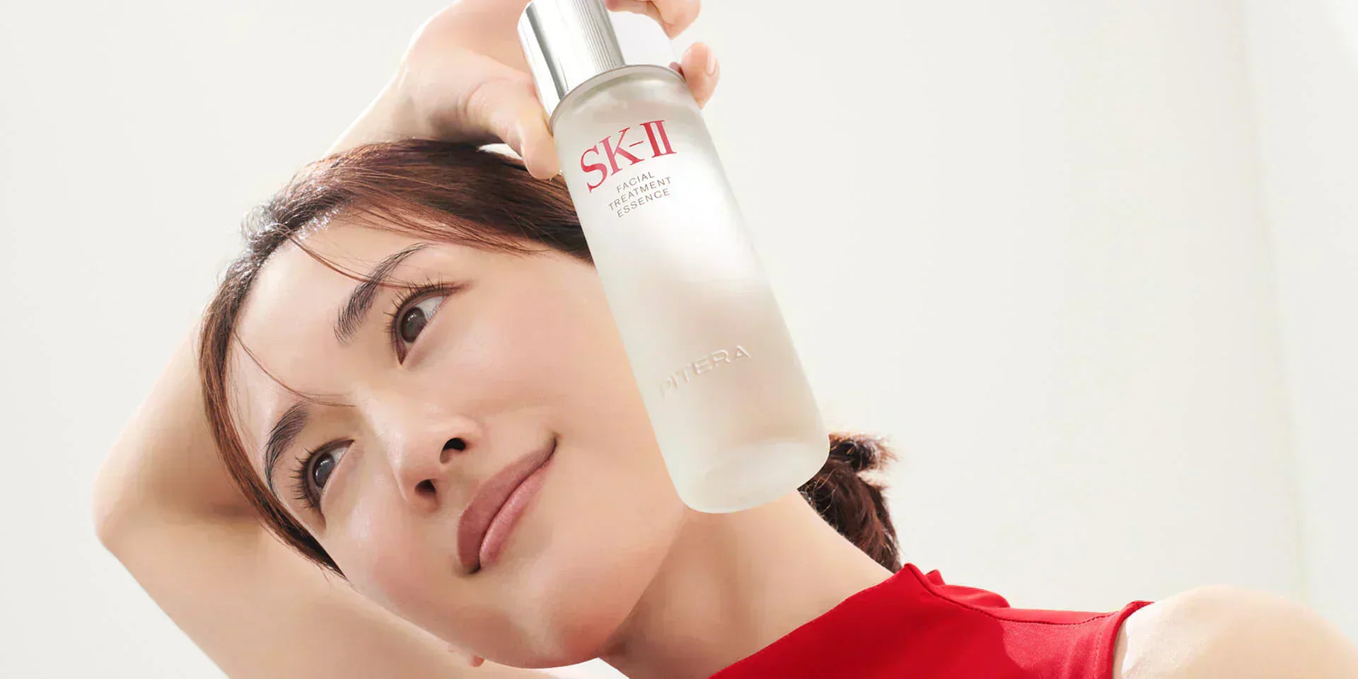 Close-up of face holding SK-II Facial Treatment Essence bottle beside cheek, representing anti-aging skincare  