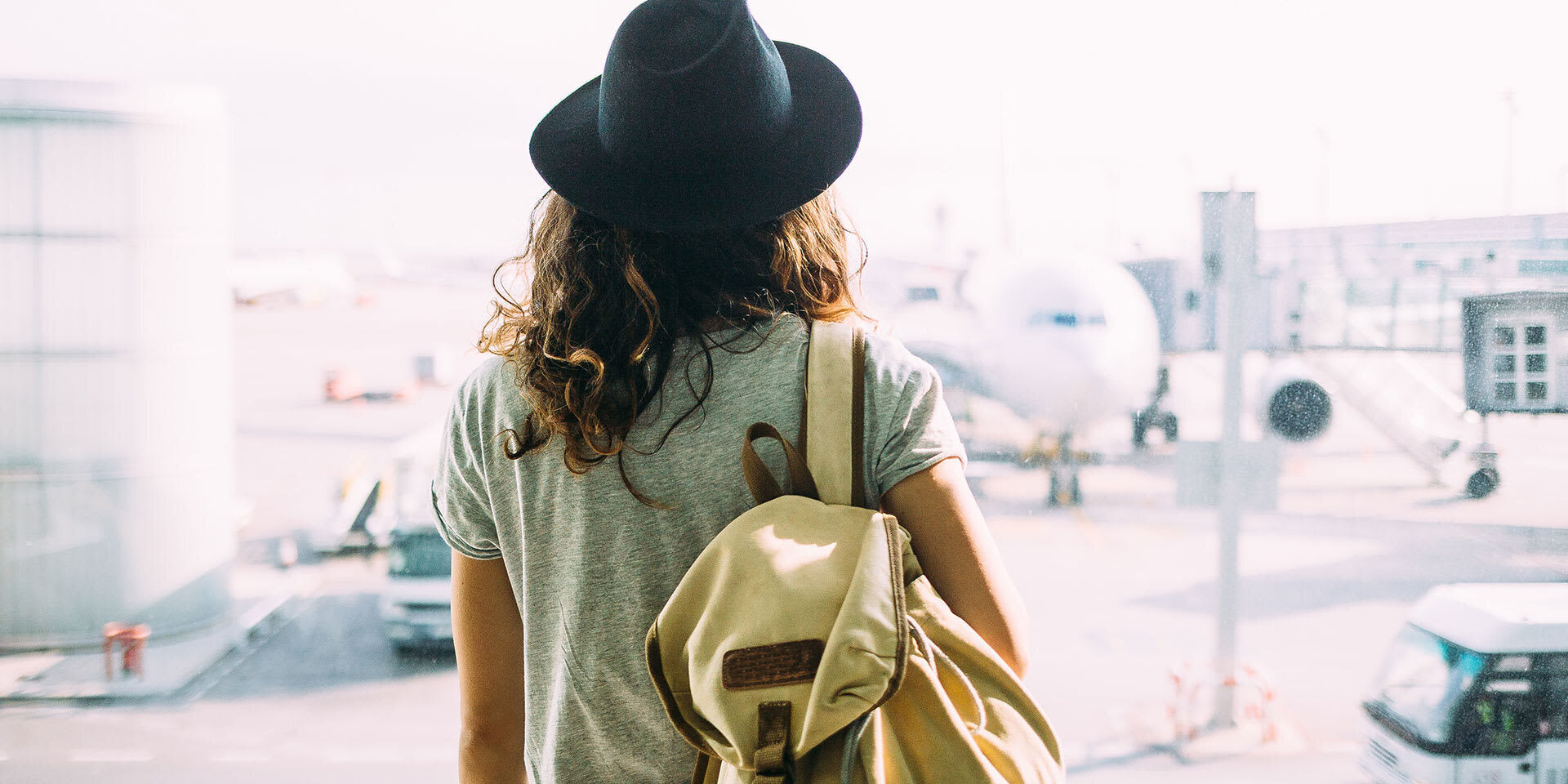 Woman standing near a window with a backpack, looking out toward aircraft at an airport terminal  