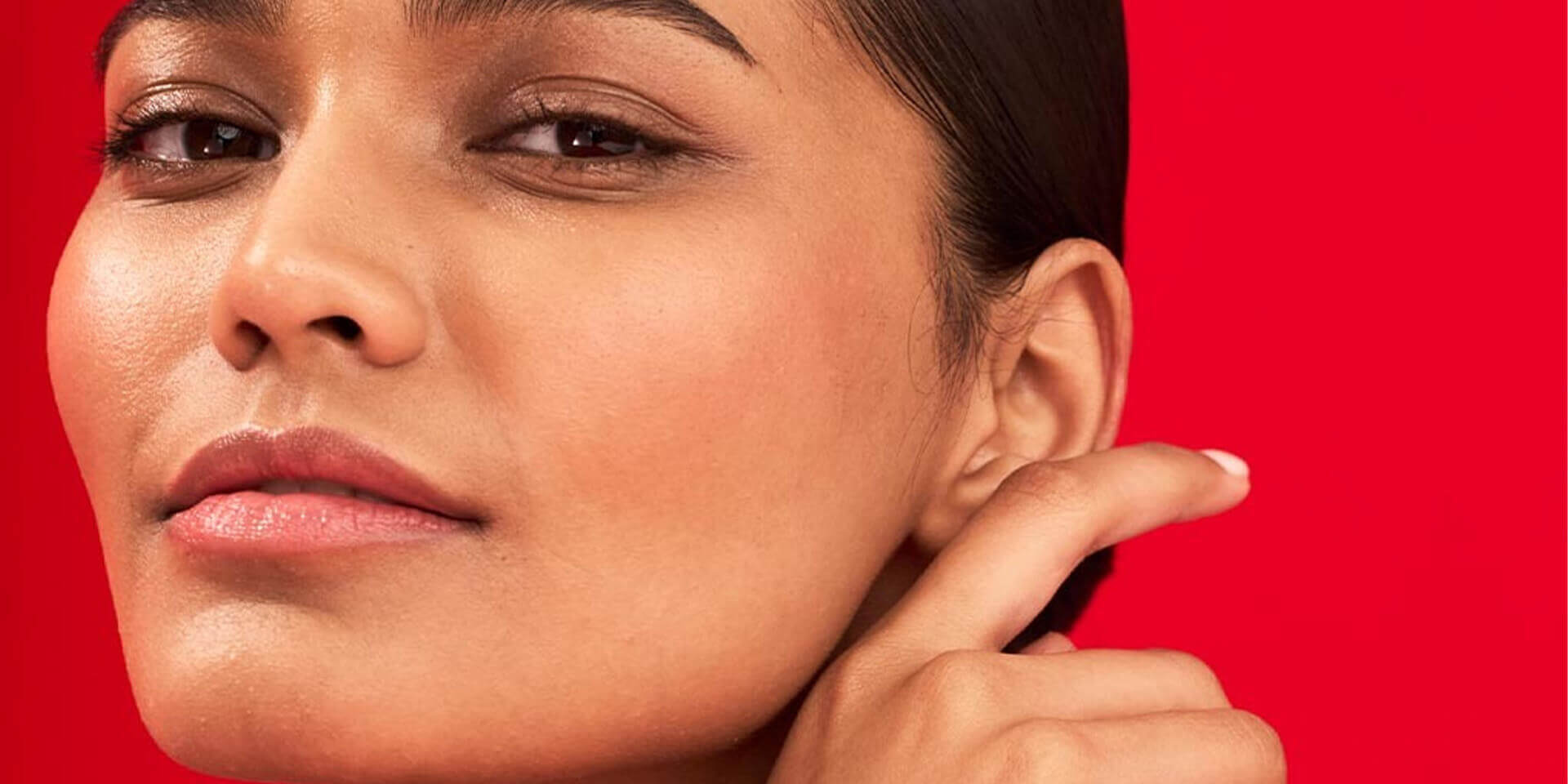 Close-up of woman showcasing facial skin firmness touching her jawline against a red background