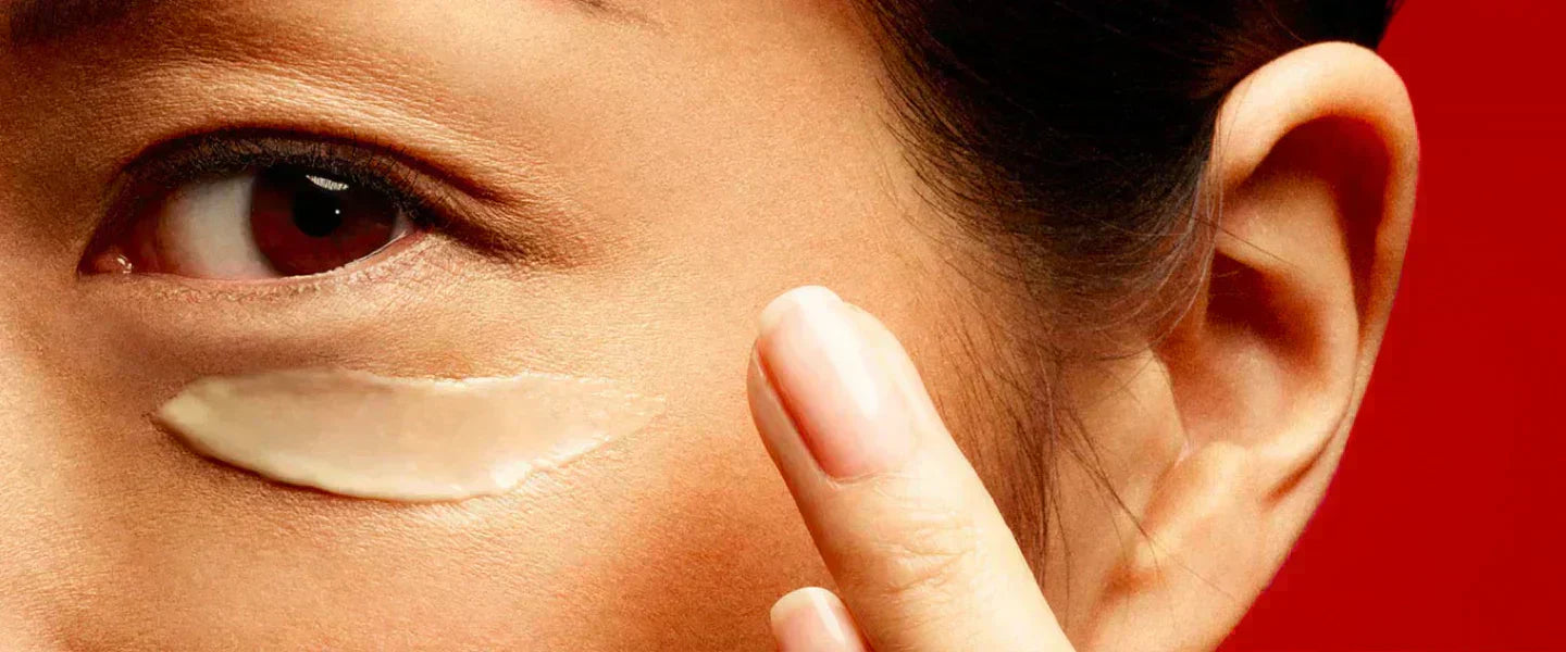 Woman applying SK-II Skinpower Eye Cream under the eye area against a red background