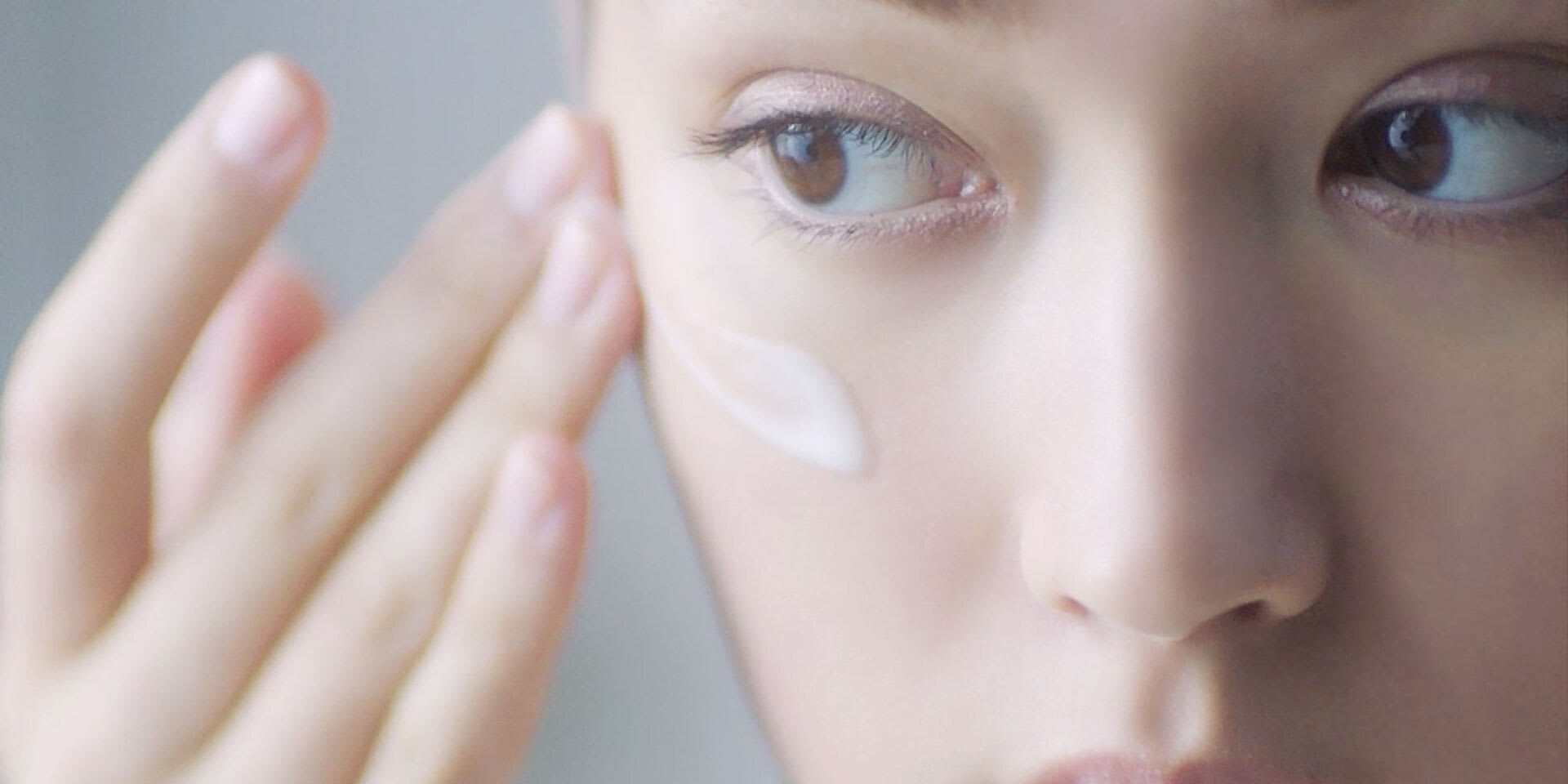 Close-up of eye area with cream applied under one eye and hand reaching toward the face