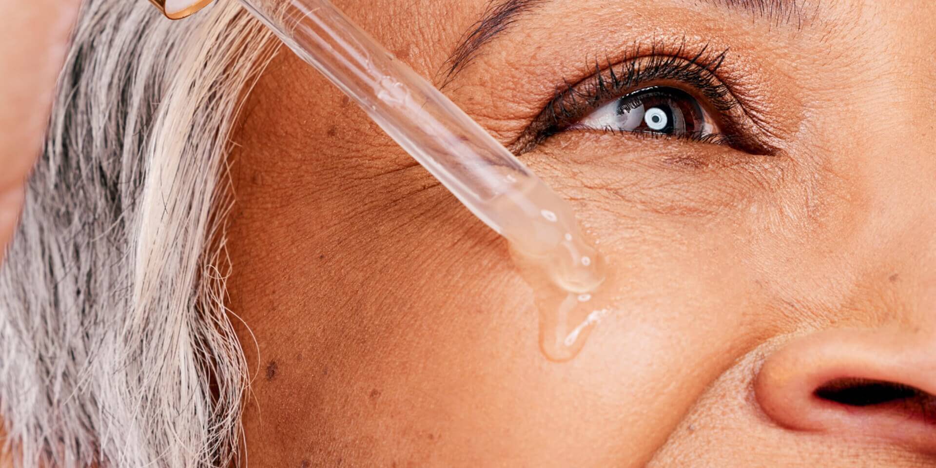 Close-up of facial skin near the eye with a dropper releasing liquid serum onto the cheek area