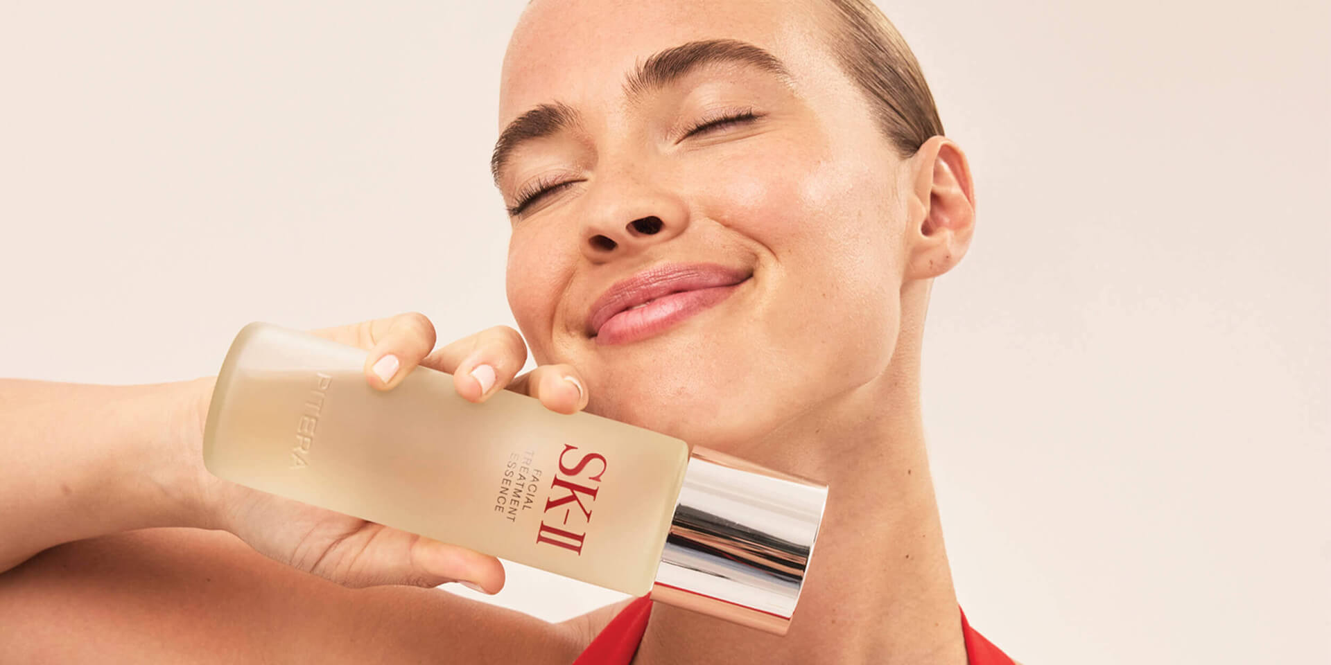 Close-up of face holding SK-II Facial Treatment Essence bottle near cheek on light background