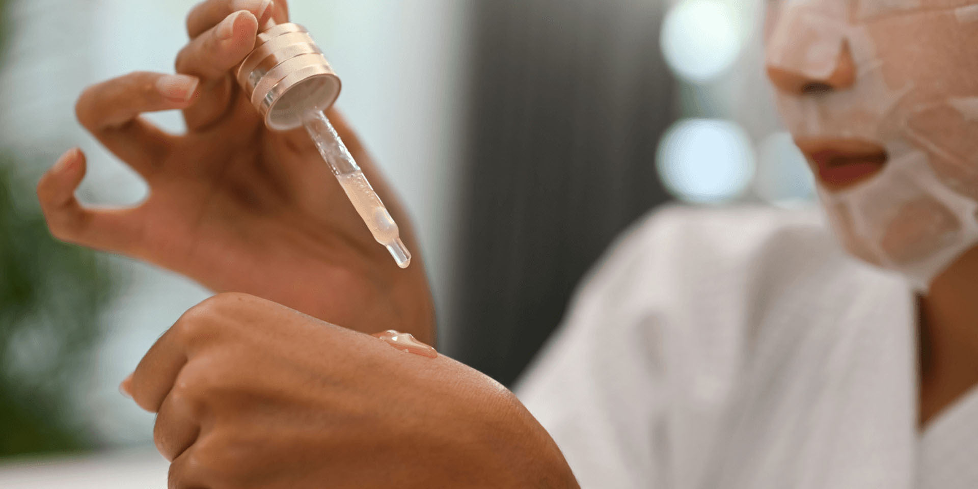 Hand holding a dropper dispensing retinol serum onto another hand, with liquid visible on skin and a blurred background