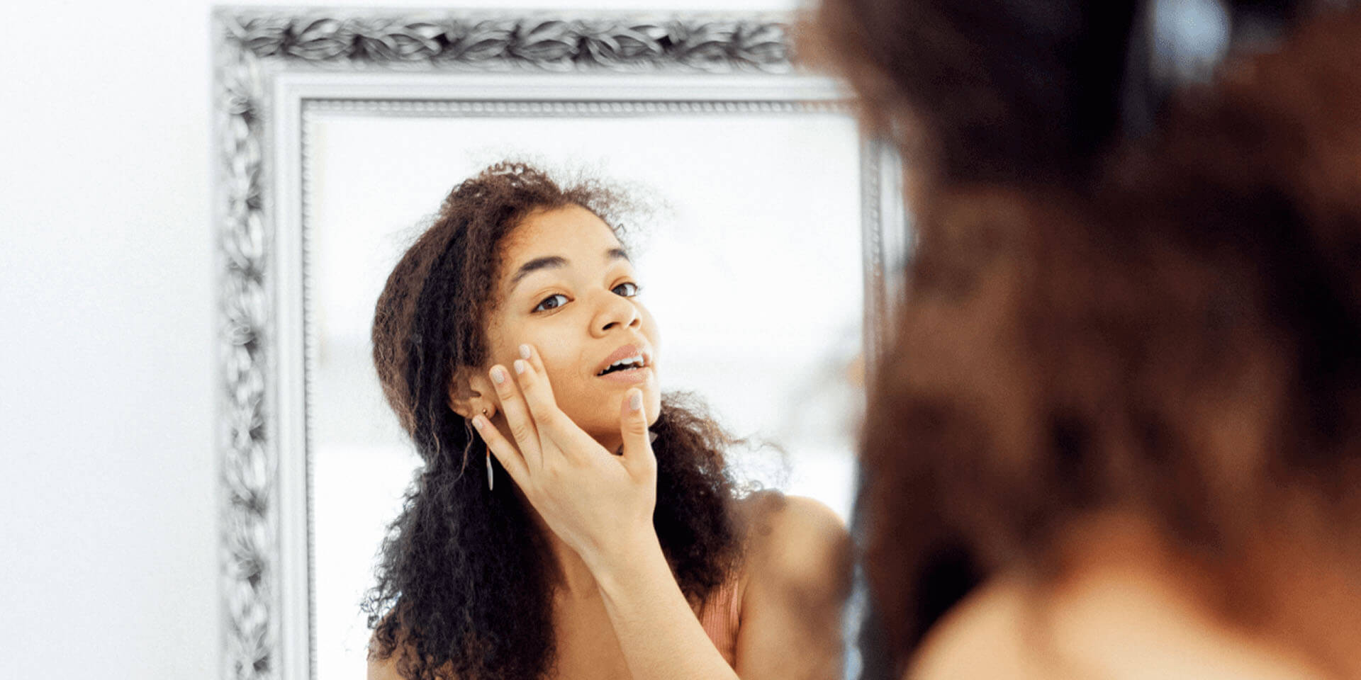 Woman looking into a mirror applying product to cheek, representing skin cycling routine