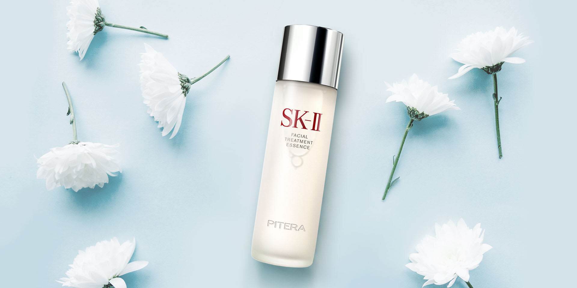 SK-II Facial Treatment Essence bottle on a blue background surrounded by white flowers in a flat lay arrangement