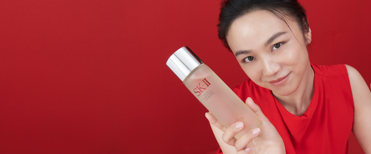 Close-up of model holding SK-II essence bottle on a solid red background