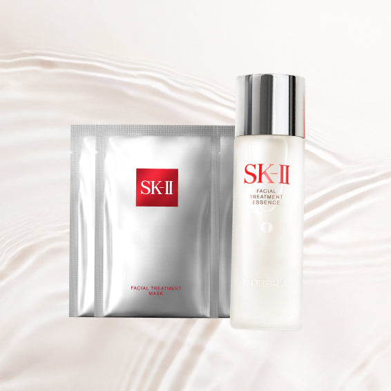 SK-II Glow Up Duo with Facial Treatment Essence bottle placed beside three sheet mask packs on a soft flowing liquid background