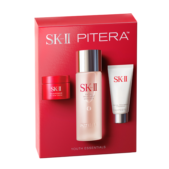 SK-II Pitera Youth Essentials Kit products including Facial Treatment Essence bottle, Skinpower cream jar, and cleanser tube arranged on a soft liquid-textured background