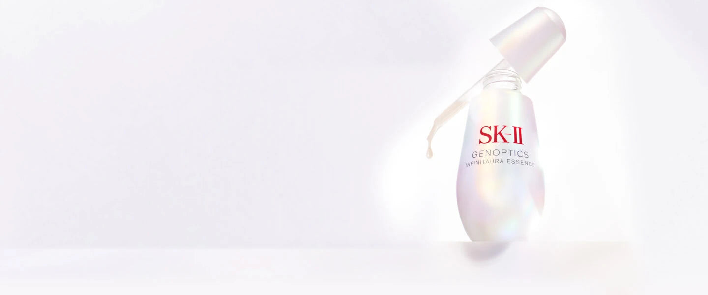 SK‑II GenOptics InfinitAura essence bottle with dropper, placed on a light surface against a soft white background