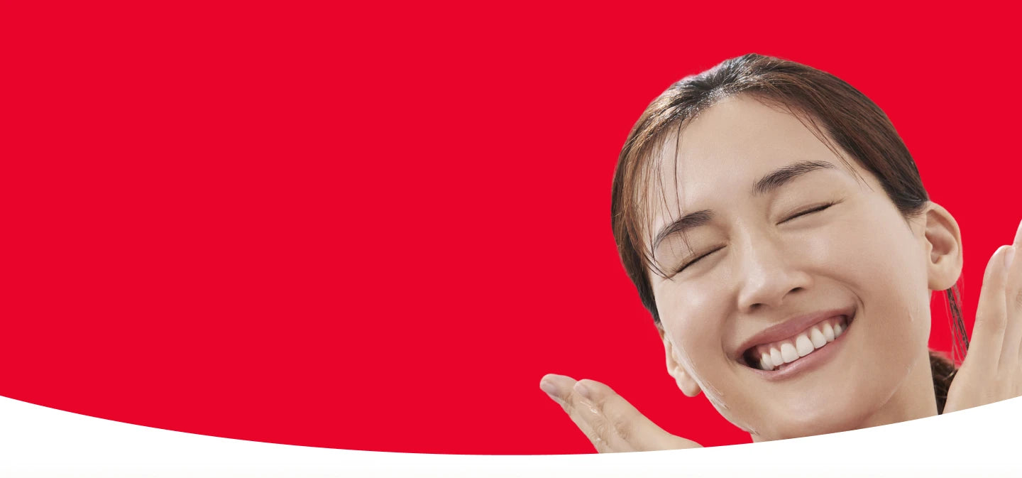 Close-up portrait of a woman with eyes closed and visible teeth against a solid red background
 