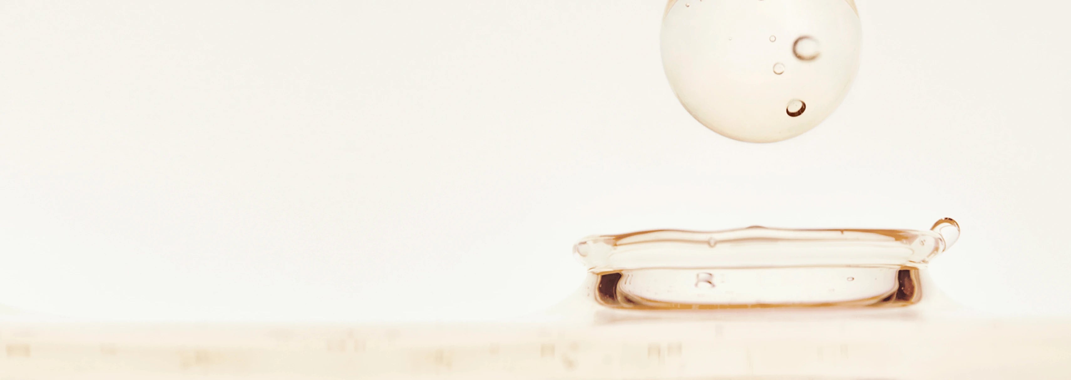Close-up of translucent liquid droplet with smaller bubbles suspended inside on a smooth liquid surface